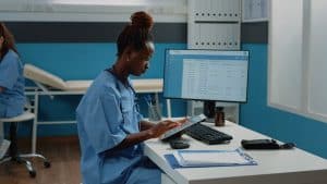 Nurse in Kenya using hospital compliance software on a tablet to review patient notes for SHIF compliance.